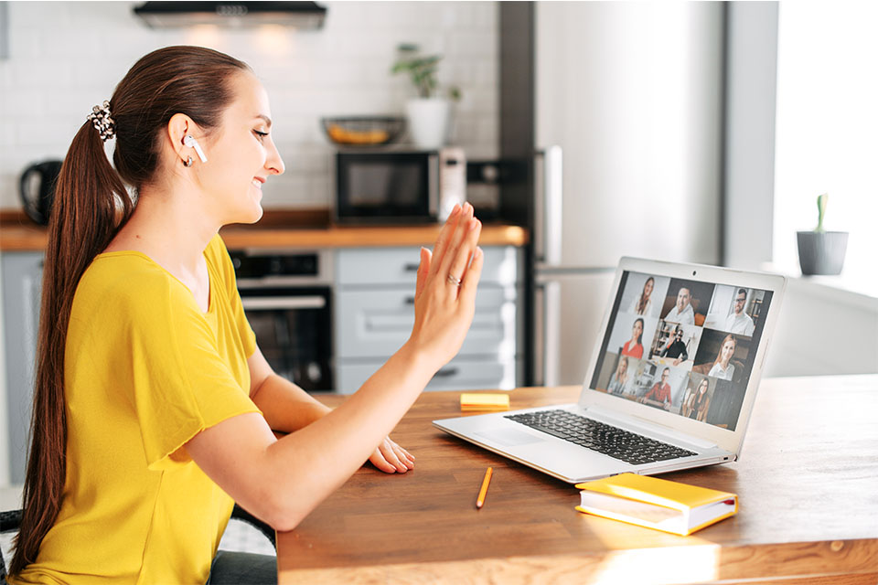 Woman greets coworkers on laptop video call.