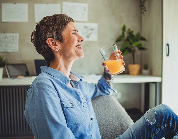 A woman relaxes on a couch, enjoying a refreshing glass of orange juice in her hand.