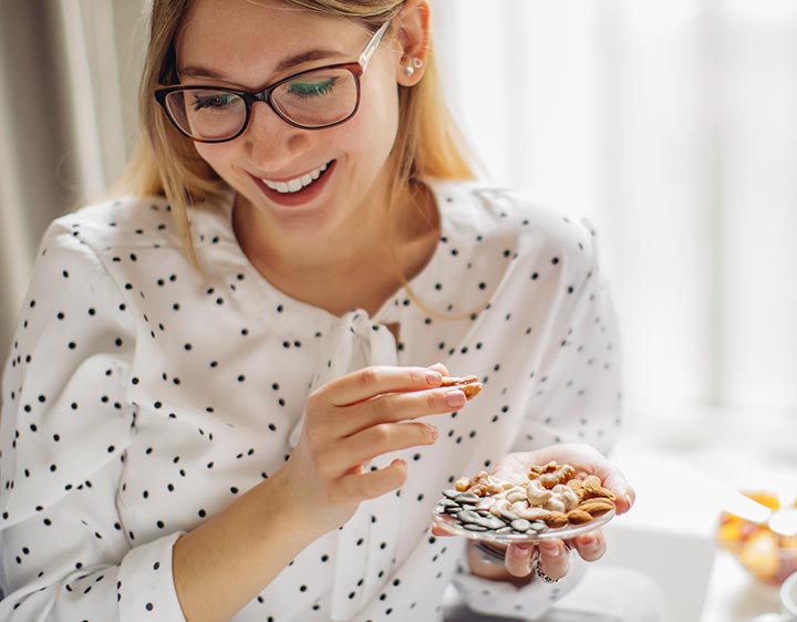 A woman wearing glasses enjoys a variety of nuts and food, highlighting the importance of vitamin E in her diet