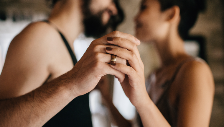 Couple hold hands while lying in bed.