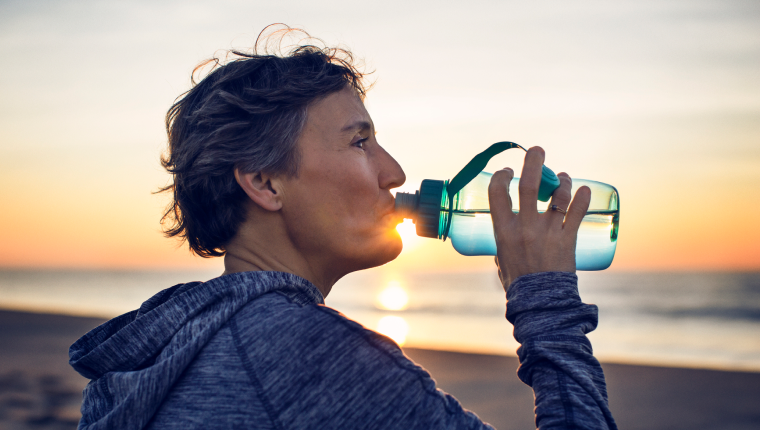 Jogger drinks water by beach.